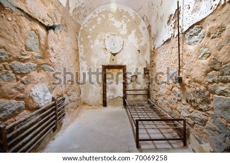 deteriorated prison cell walls and rusty metal bed frame