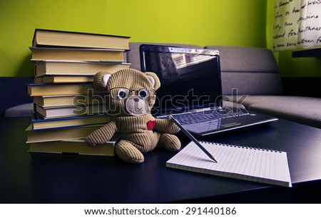 Close up of teddy bear writing down some notes. Notebook and books in the background.