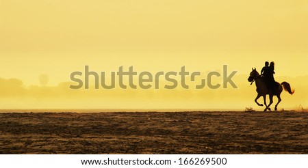 Man and woman riding a horse at sunrise
