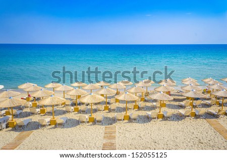 Panoramic view of straw umbrella on an empty beach with a perfect clear blue water and sky horizon at distance.
