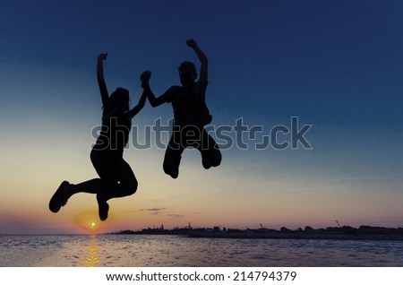 Silhouette Couple Girl and boy jumping on the beach sunset water horizon and clear colorful sky