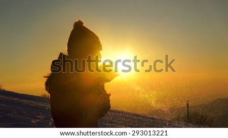 Young female silhouette blowing snow on sunset