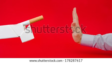 No smoking suggested by a business man refusing a pack of cigarettes on a red serious alerted important background with a dangerous look