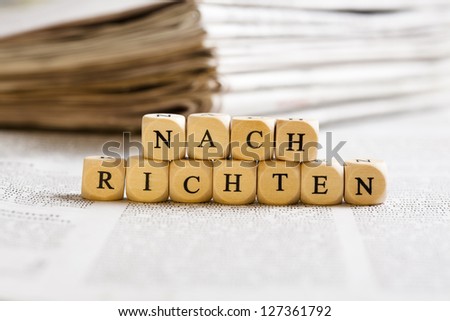 Concept of dices with letters forming word: Nachrichten (German for News). Generic newspaper background with some blurred text on the bottom and paper stack in the back.