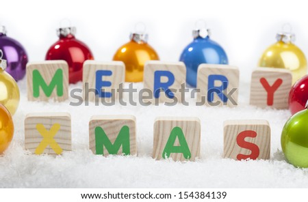 Merry Xmas text in front of Christmas decoration baubles in different colors on a (artificial) snow ground.