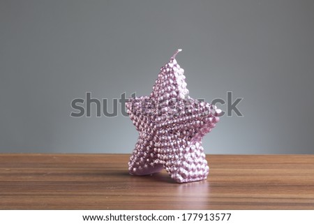 Single purple candle in shape of a star on a wooden table.