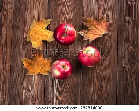 Autumn border from apples and fallen leaves on old wooden table.