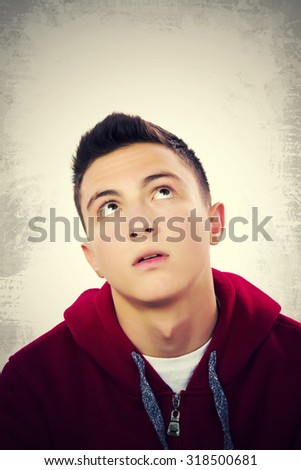 Portrait of handsome teenage boy thinking and lloking up to empty space. Grunge background.