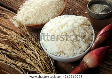 cooked rice, uncooked rice and paddy rice on wooden table; three varieties of rice