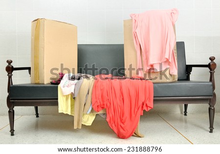 cardboard boxes and stack of clothes on a black sofa in living room