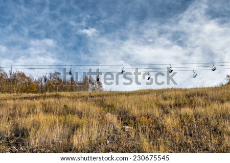 A ski chair lift sits empty over an alpine meadow during autumn with wispy clouds overhead.