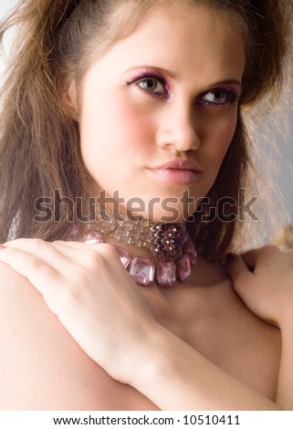 Young beautiful woman with stylish make-up and neck-lace put her hands on bare shoulders