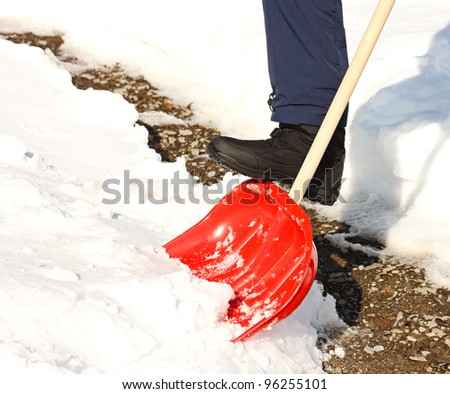 Close-up of man shoveling snow with red shovel.Cleaned path in background.
