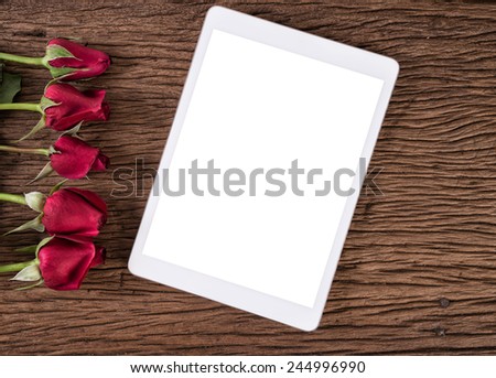 Tablet computer and red rose on old wooden background