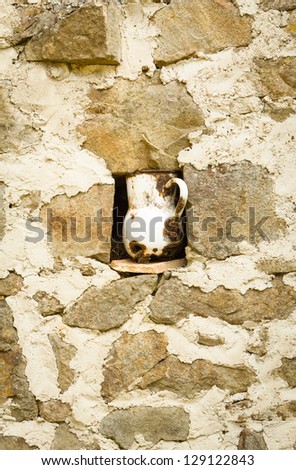 Detail of vintage metallic pitcher in a niche in stone wall