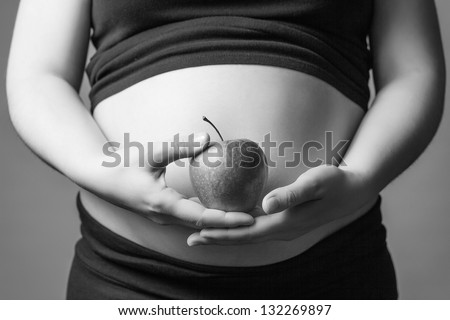 Closeup of pregnant belly woman, holding a red apple in her hands