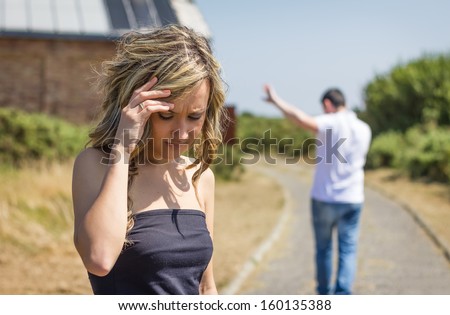 Unhappy frustrated woman in focus and angry man leaving on the background after quarrel