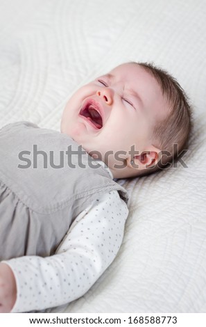 Cute baby girl crying over white bedcover