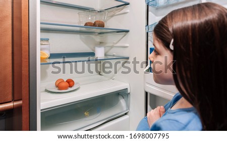 Worried girl looking at the almost empty fridge due to a crisis