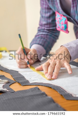 Woman dressmaker drawing tailor pattern with pencil for a suit on the table