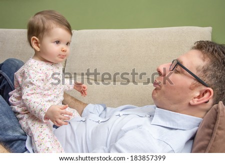 Portrait of happy father playing with cute baby sitting over his belly in a sofa at home