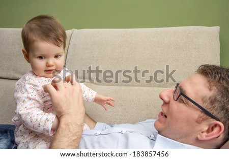 Portrait of happy father playing with cute baby sitting over his belly in a sofa at home