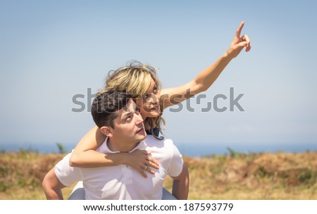 Happy handsome guy carrying his girlfriend on the back outdoors in a summer day over nature background