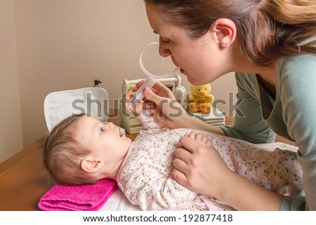 Mother cleaning mucus catarrh of adorable baby with a nasal aspirator