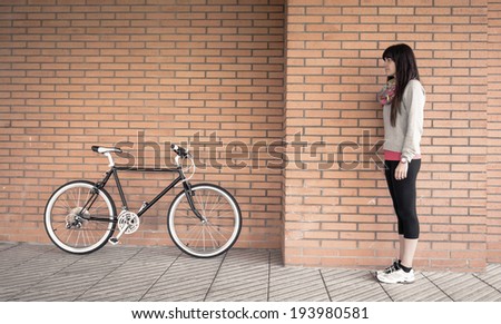 Beautiful young sportive woman posing with custom fixie bike over a orange brick wall on the background