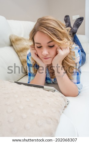Portrait of beautiful teenager using tablet pc lying down on a sofa. Home relax, leisure and technology concept.