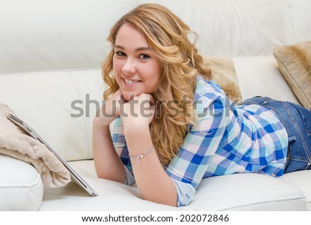 Portrait of beautiful teenager using tablet pc lying down on a sofa. Home relax, leisure and technology concept.