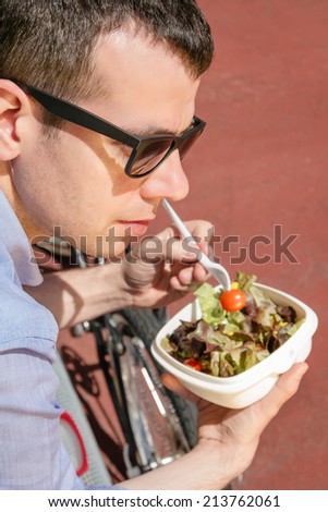 Young business man eating a salad at lunch break sitting on a bench outdoors