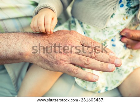 Baby girl touching hand of senior man. Two different generations concept.