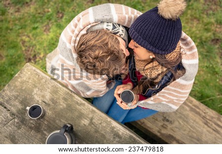 View from above of young couple under striped blanket and with hot beverage kissing outdoors in a cold day