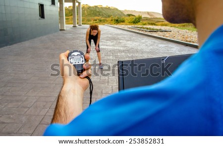 Closeup of man trainer hand using a chronometer to timing at tired athletic young woman in a hard training outdoors