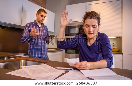 Angry young couple arguing by their many debts at home. Financial family problems concept.