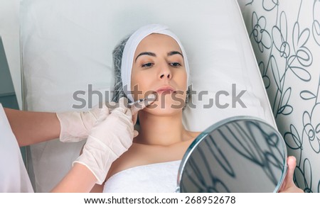 Young pretty woman looking a beauty lips treatment in a mirror. Medicine, healthcare and beauty concept.