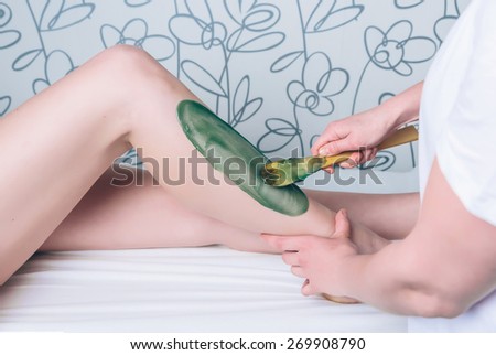 Closeup of beautician hands doing depilation to beautiful woman legs with hot wax in a beauty salon