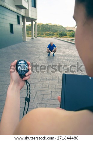 Closeup of woman trainer hand using a chronometer to timing at tired athletic man in a hard training outdoors