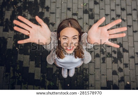 Top view of happy young trendy woman raising her hands up over a gray street paving stone background