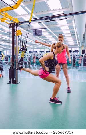 Female personal trainer teaching to woman in a hard suspension training with fitness straps on a fitness center