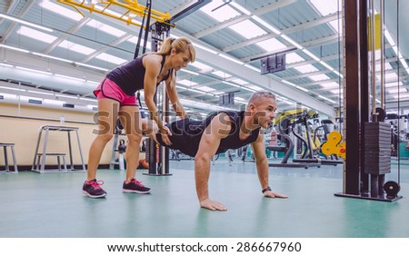 Female personal trainer teaching to man in a hard suspension training with fitness straps on a fitness center