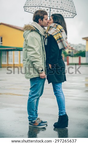Portrait of young beautiful couple kissing under the umbrella in an autumn rainy day. Love and couple relationships concept.