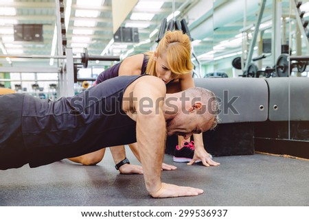 Woman personal trainer encouraging to muscle man during a hard push ups training day on fitness center