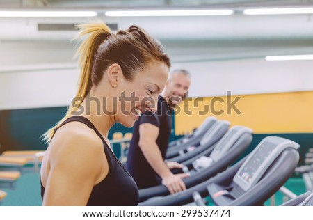 Beautiful fitness woman laughing with friend in a treadmill training on fitness center