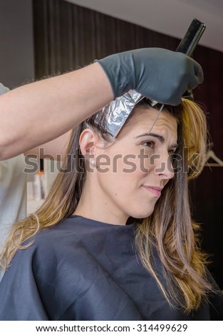 Hairdresser separating strands of hair of beautiful young woman with aluminium foil in the process of hair color change