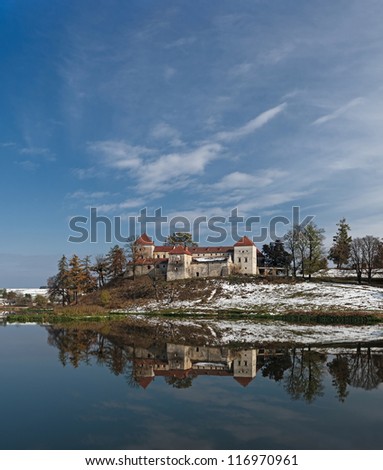 Huge panorama of Svirzh medieval castle, reflected in water of nearby lake under high blue sky with clouds