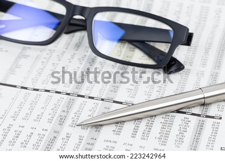 Pen and glasses rest on stock price detail financial newspaper