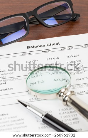 Balance sheet financial report with pen, glasses, and magnifier; document is mock-up