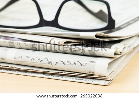 Stack of business newspapers on table with glasses